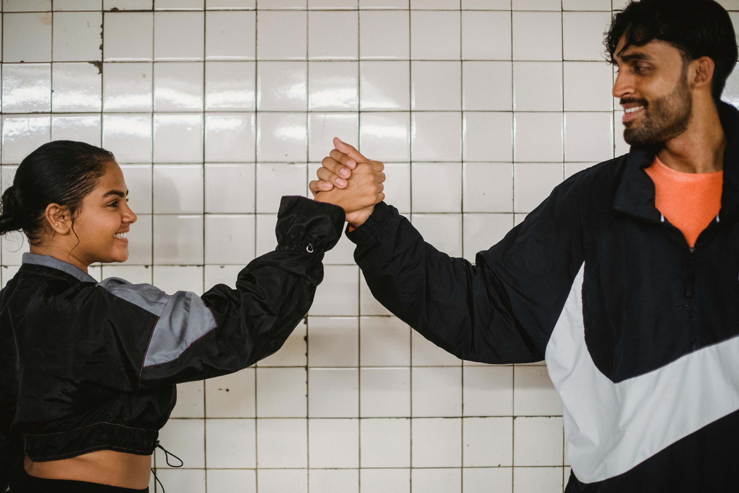 Two young adults in sportswear shaking hands, expressing teamwork and cooperation.